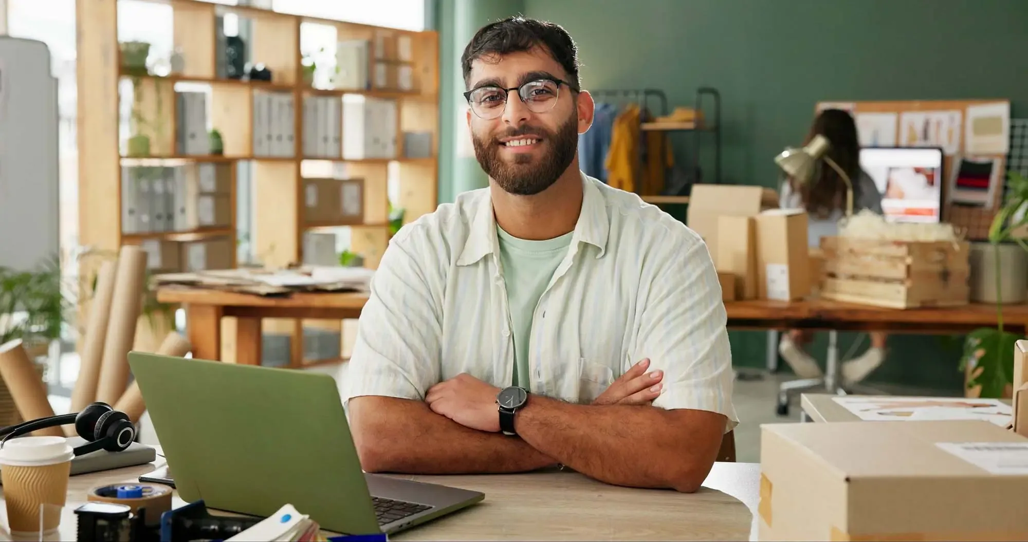 An online store owner at his laptop in a small fulfilment studio, with packed orders ready to ship behind him