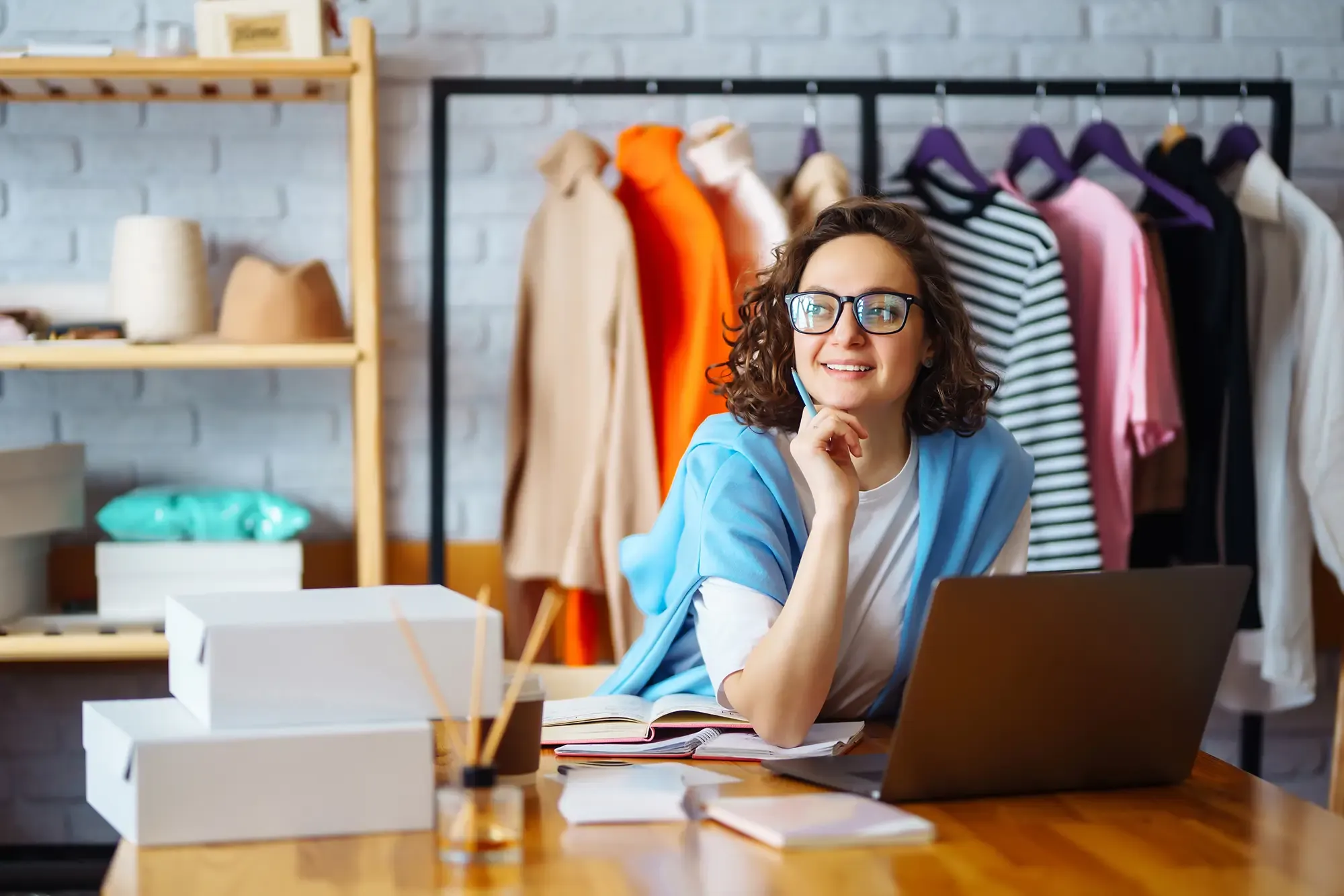 A WooCommerce shop owner working on her online store from her laptop, surrounded by stock and packed orders